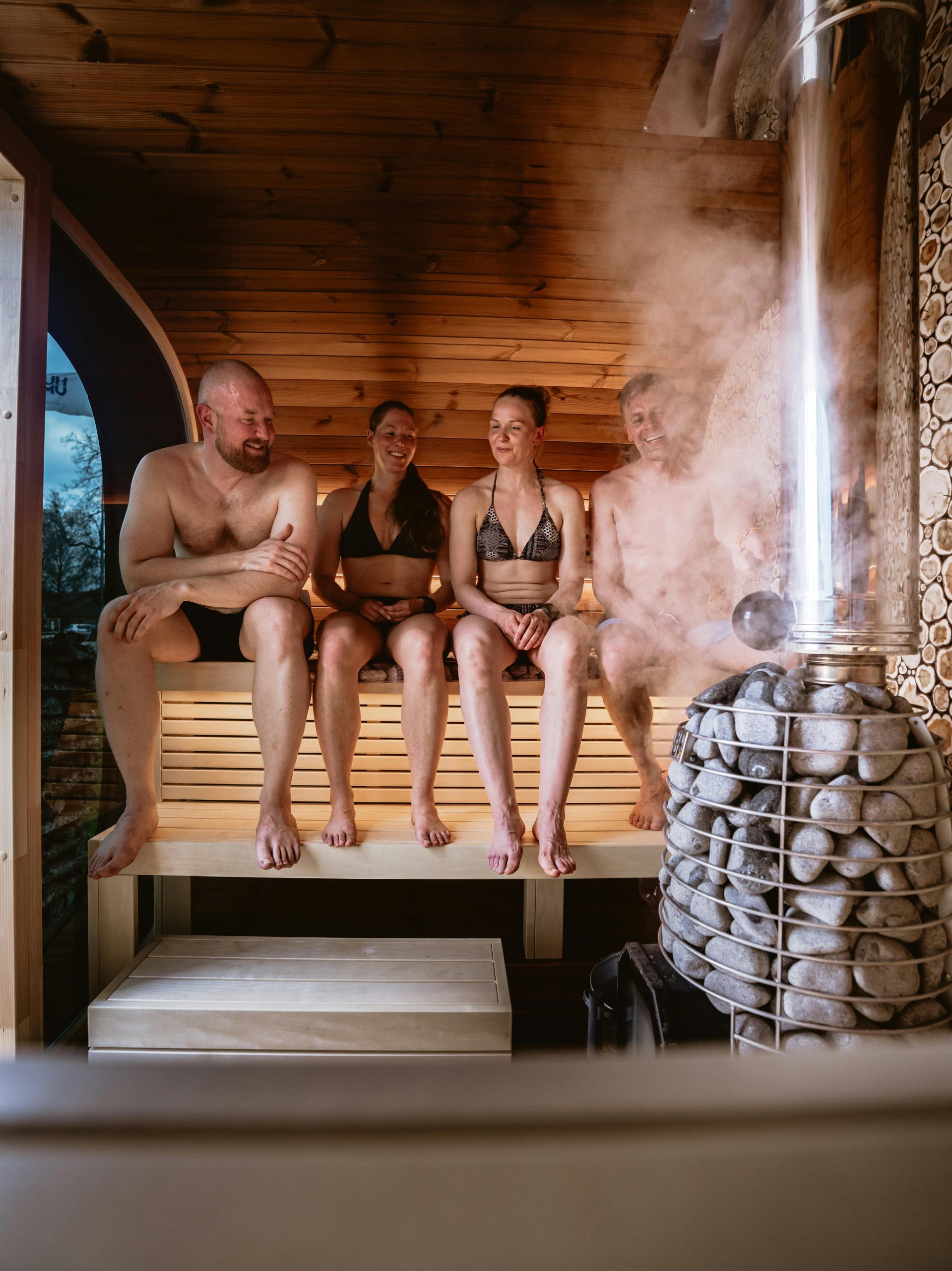Group enjoying a relaxing sauna with steam from wood stove and stones.