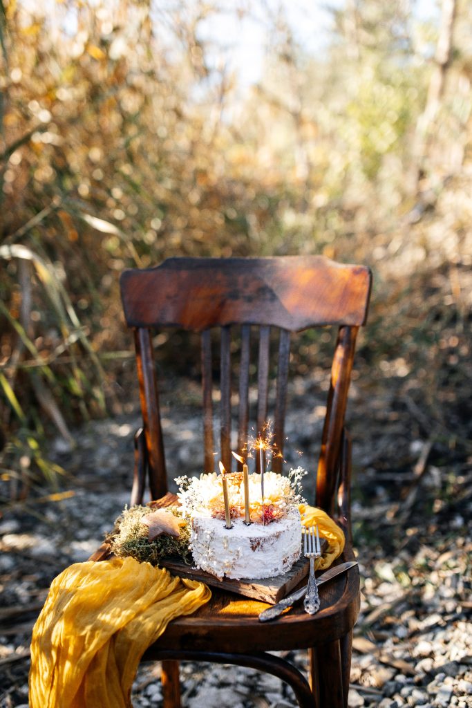 A rustic homemade cake with sparklers on a wooden chair in an autumn setting, perfect for celebrations.